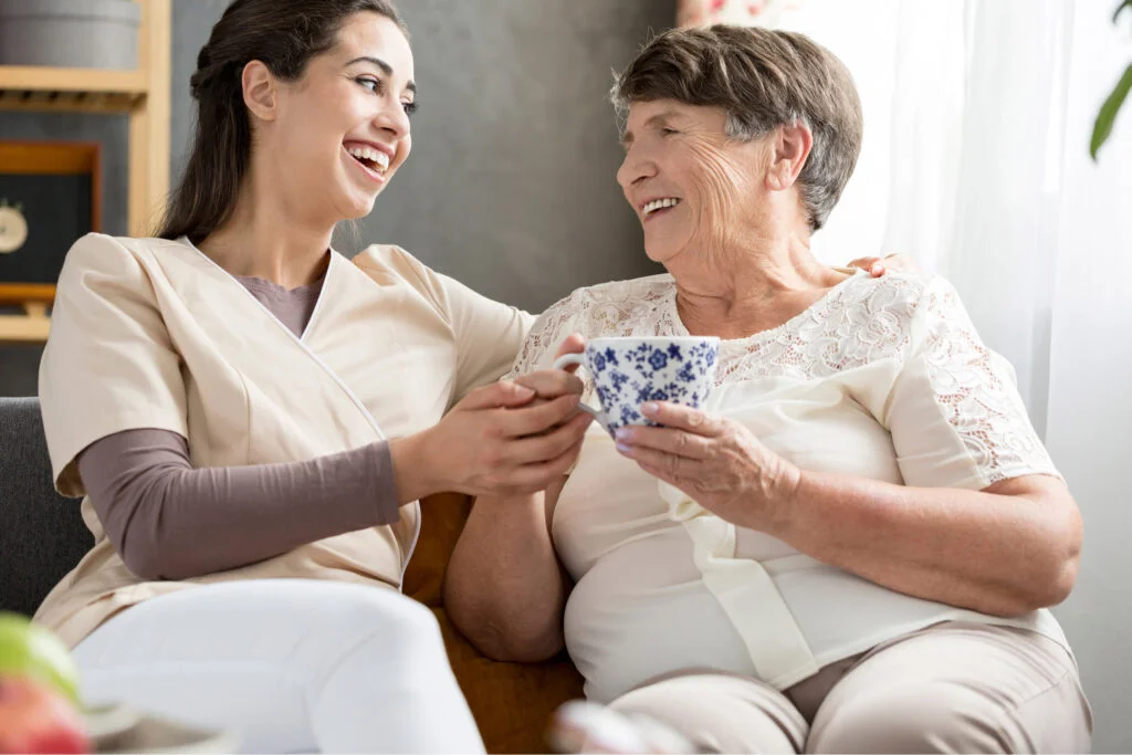 older and younger woman smiling and sat close to each other. Atwell Care Ltd. Live in care. Home Care. Care Company. Bath. Frome. Keynsham. Saltford.