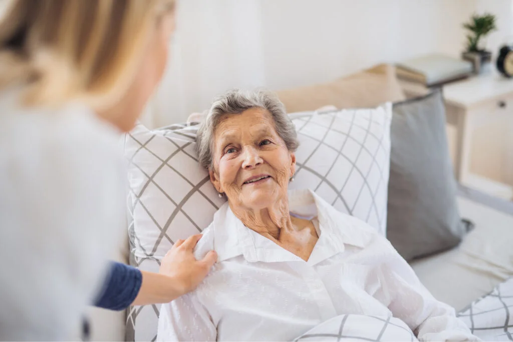 Smiling woman laying on her bed, looking at woman in front of her. Atwell Care Ltd. Live in care. Home Care. Care Company. Bath. Frome. Keynsham. Saltford.