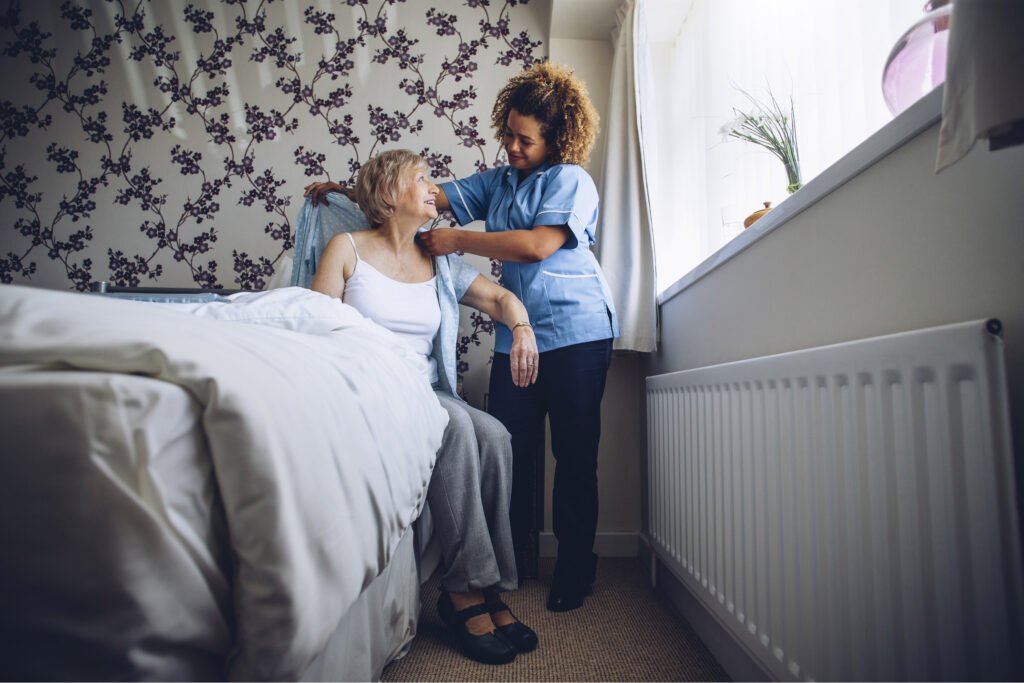 Woman carer supporting a happy old woman get dressed in her bedroom. Atwell Care Ltd. Live in care. Home Care. Care Company. Bath. Frome. Keynsham. Saltford.